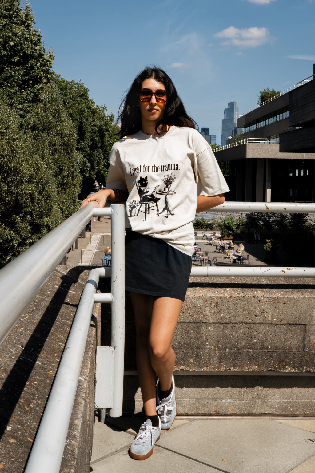Woman wearing a graphic t-shirt and sunglasses standing on a staircase with a cityscape background