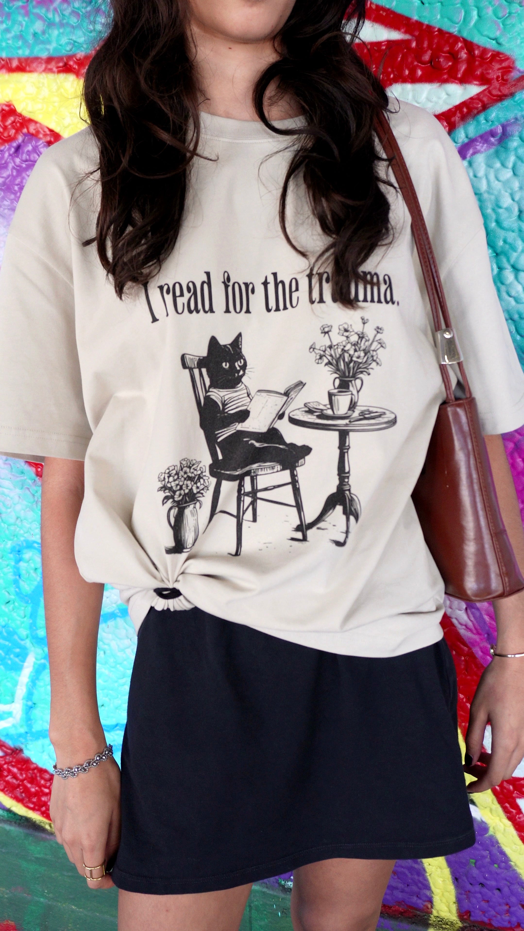 Person wearing a white t-shirt with a graphic design and text, standing against a colorful abstract background.