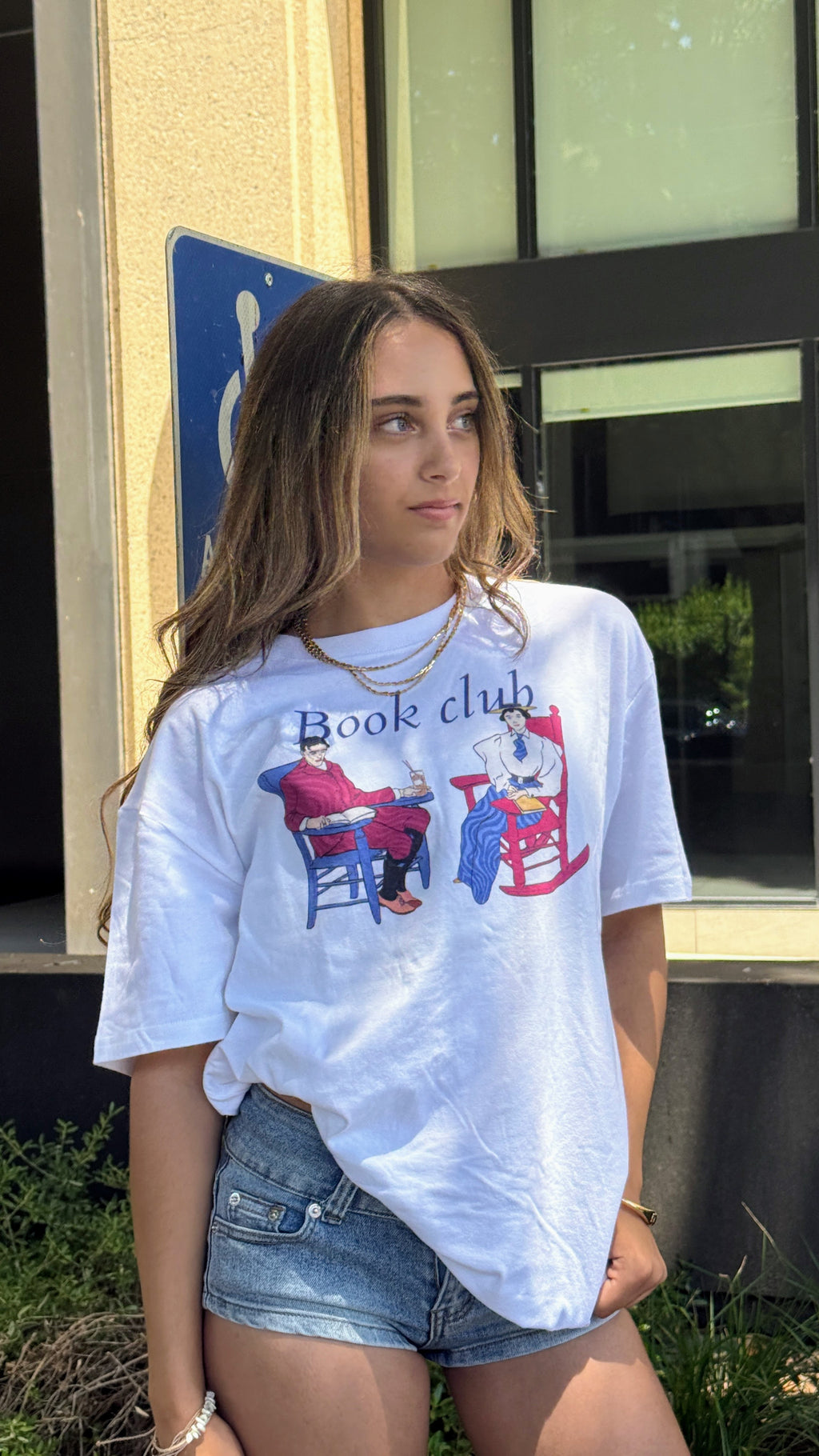 Model wearing the HANABI CLUB “Book Club Lounge” T-shirt with denim shorts outdoors.