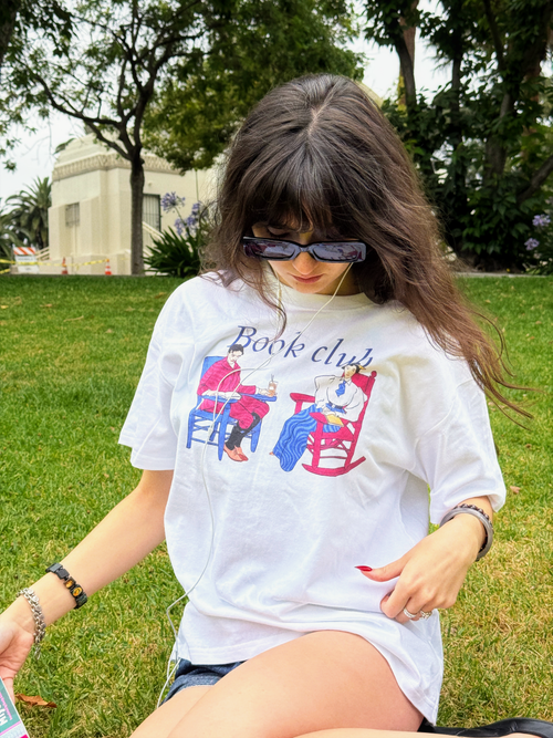Model wearing the HANABI CLUB “Book Club Lounge” T-shirt while sitting in a park.