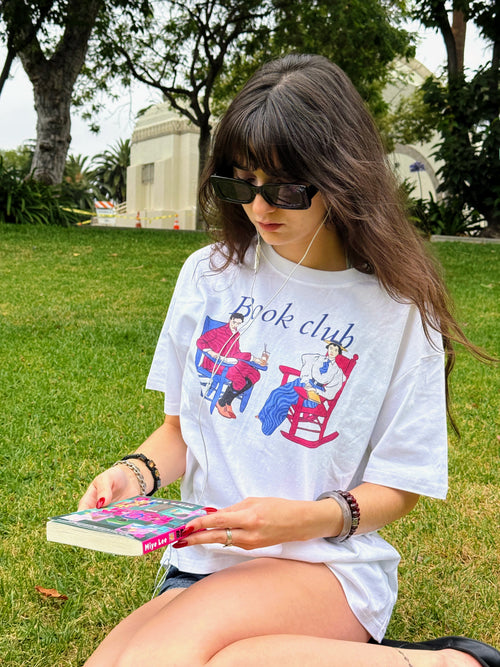 Model reading a book in a park while wearing the “Book Club Lounge” T-shirt.