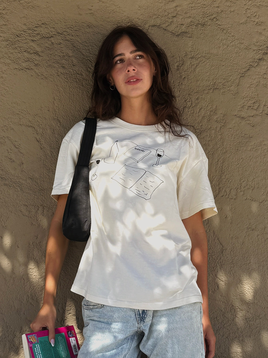 Model wearing the “Books and Wine” T-shirt with jeans while holding books outdoors.