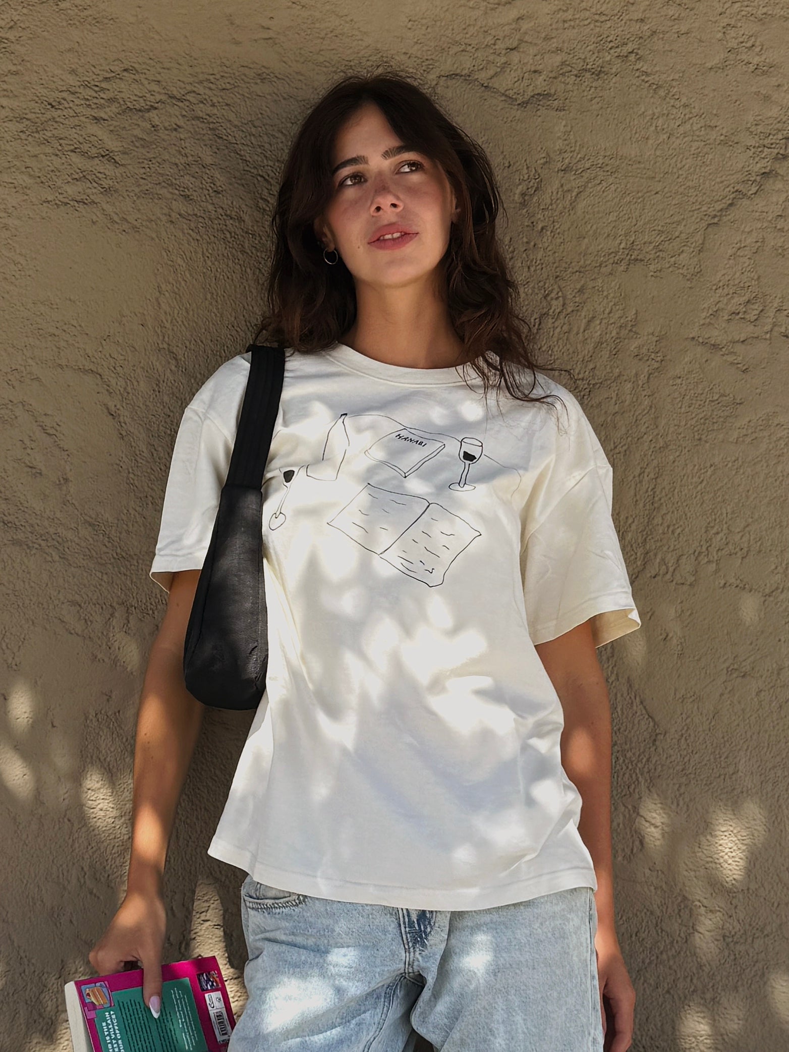 Model wearing the “Books and Wine” T-shirt with jeans while holding books outdoors.