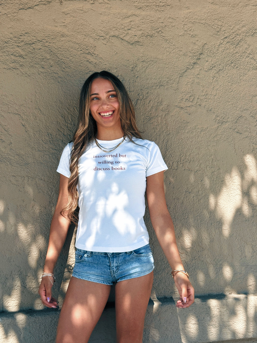 Model wearing the “Introverted but willing to discuss books” baby tee with denim shorts outdoors.