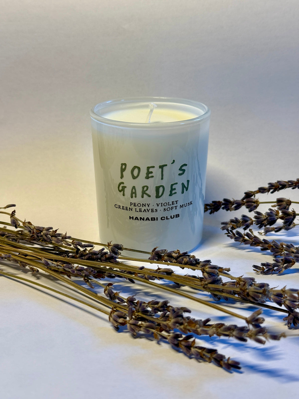 Close-up of Poet's Garden candle showing its green printed label and white wax, with dried lavender arranged around the jar.