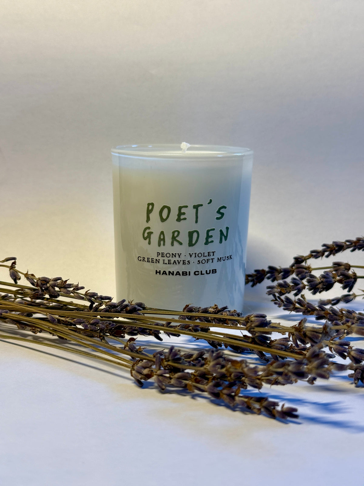 White glass Poet's Garden scented candle by HANABI CLUB, styled with dried lavender stems against a light background.