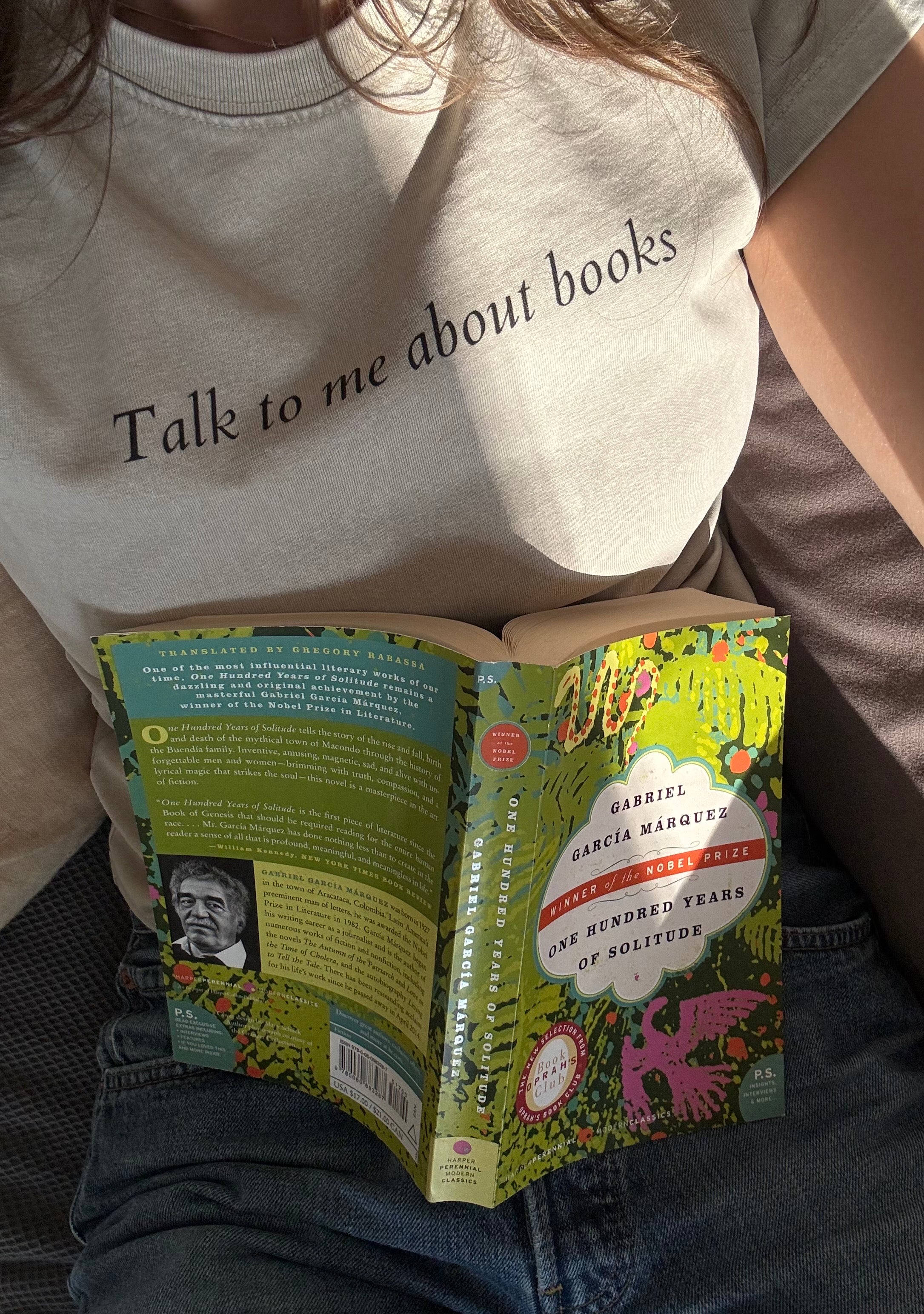 Close-up of the “Talk to me about books” ladies tee while the model reads a book.