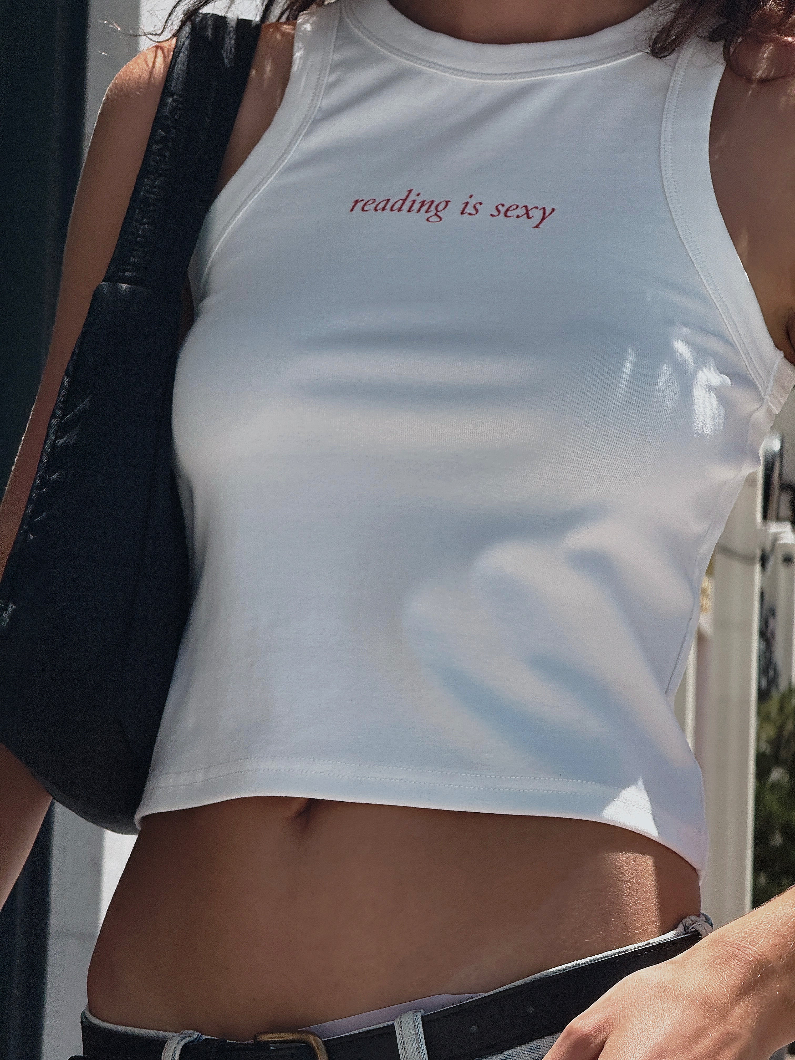 Close-up of a white HANABI CLUB “reading is sexy” tank top styled with jeans and a black shoulder bag.