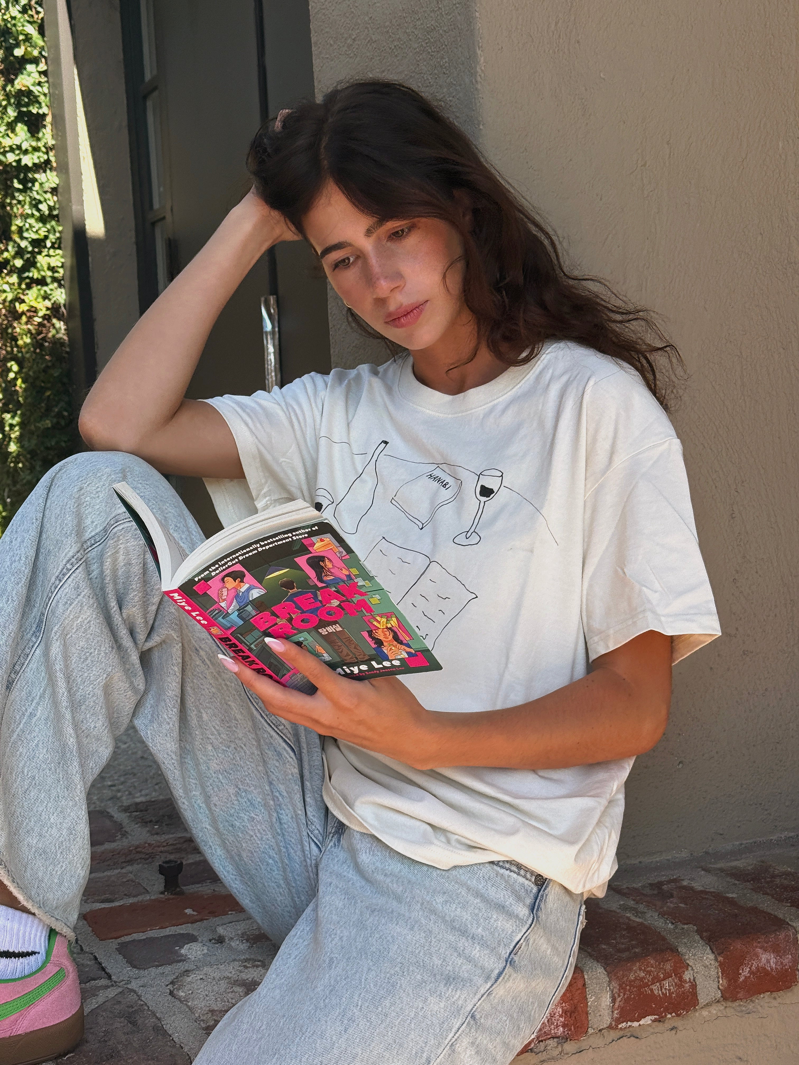 Model sitting with a book while wearing the “Books and Wine” T-shirt and jeans.