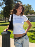 Model wearing a white fitted HANABI CLUB T-shirt that says “Talk to me about books”, styled with light-wash jeans in a park.