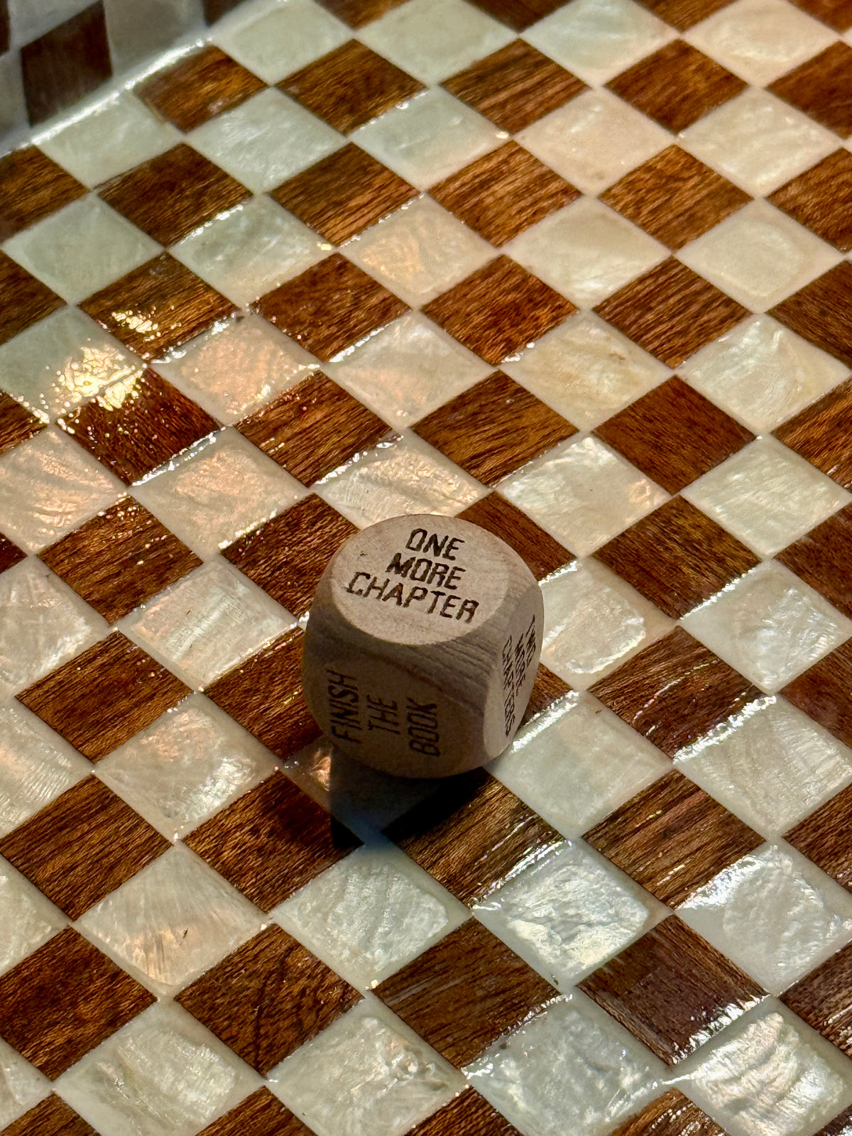 Close-up of a wooden Reading Decision Die showing One More Chapter and Finish The Book.